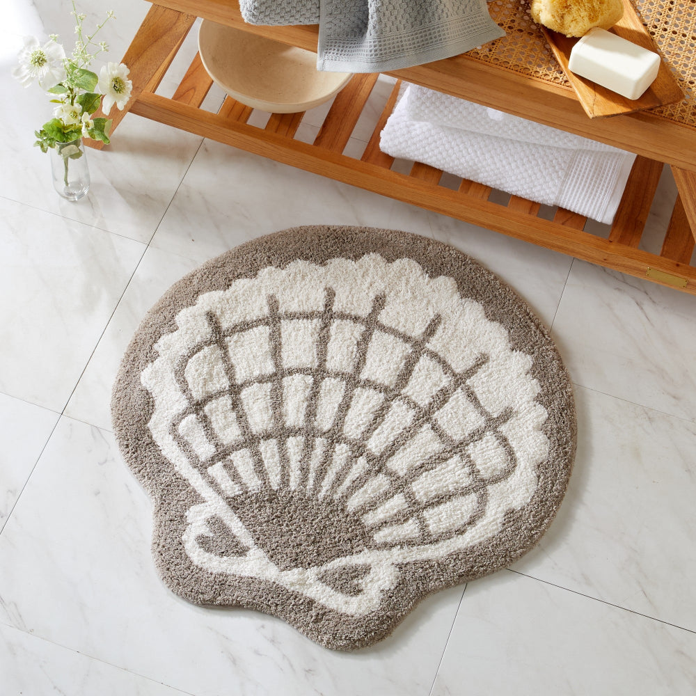 Shell-shaped bath mat on a tiled bathroom floor with a wooden shelf in the background.
