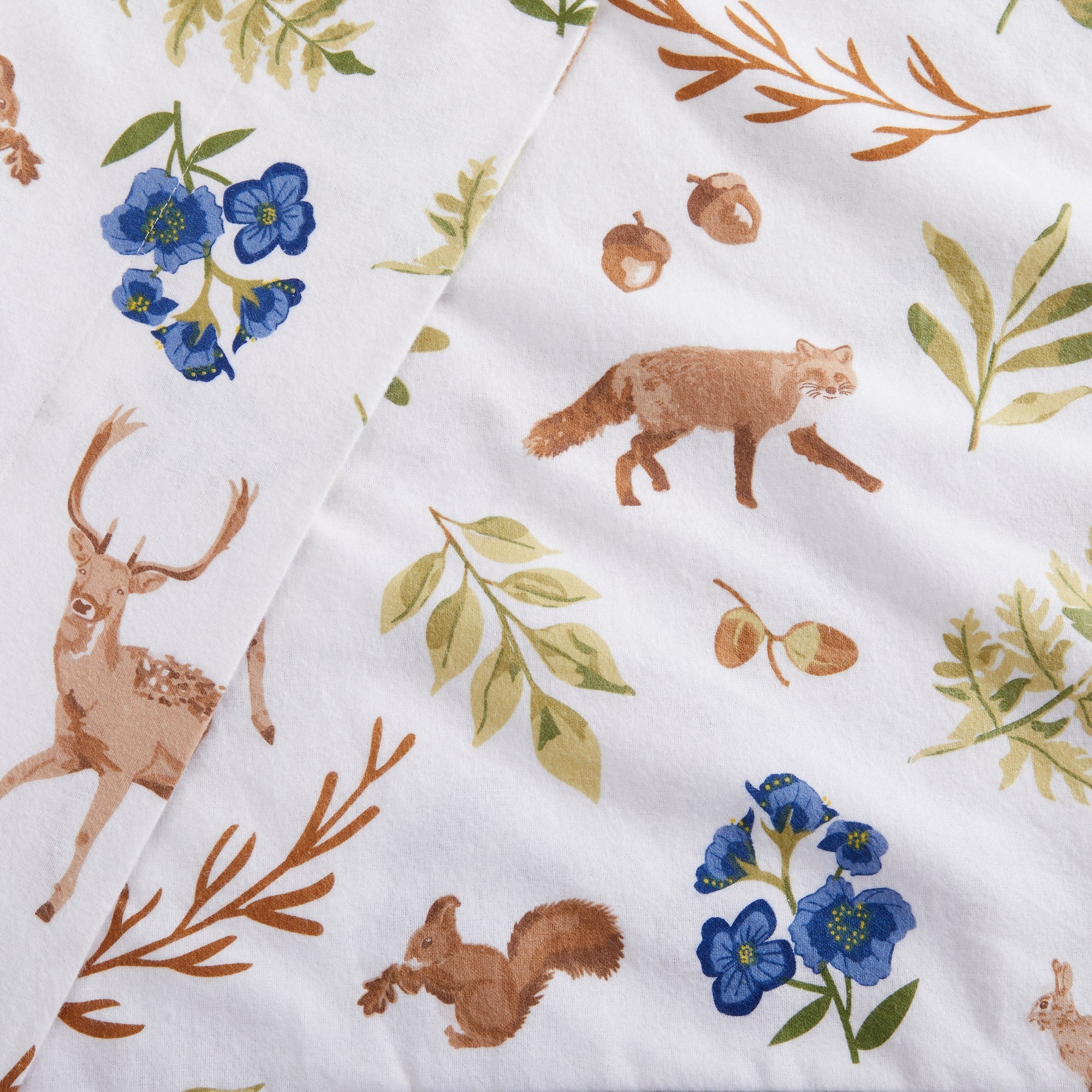 Fabric with nature-themed prints including deer, flowers, and leaves on a white background.