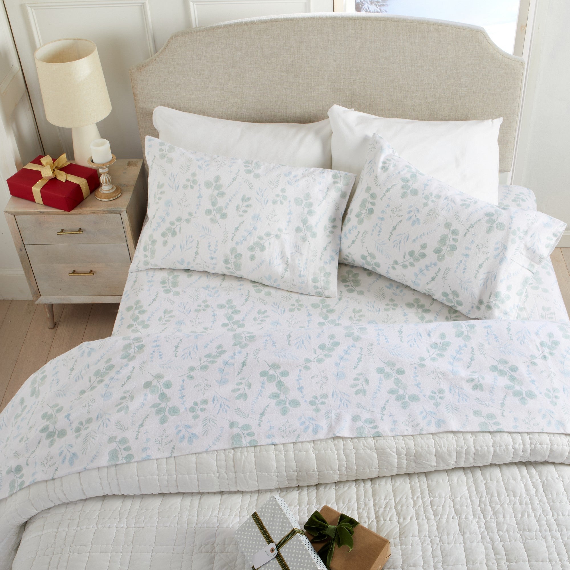 Floral-patterned bedding set on a bed with a nightstand and gift box in the background.