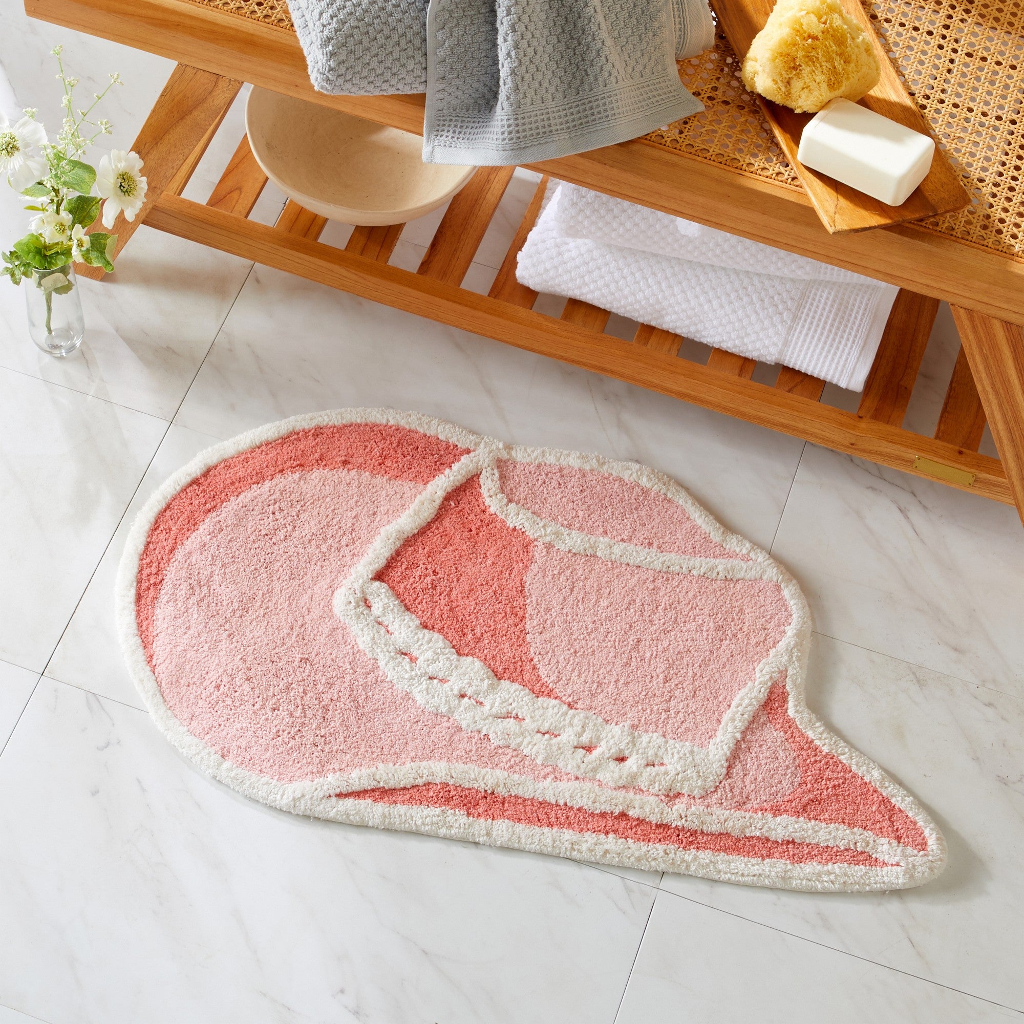 Pink and white bath mat on a tiled floor with a wooden shelf in the background.