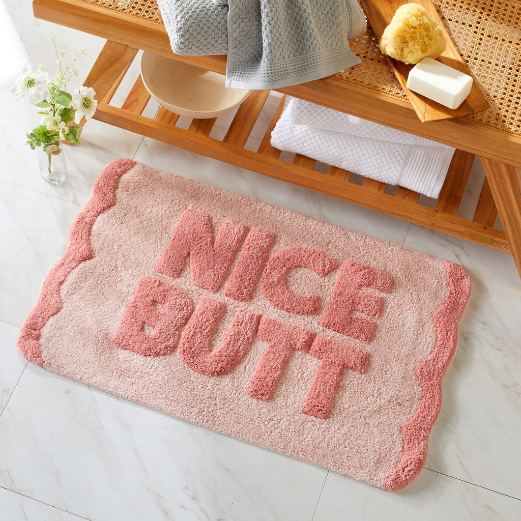Pink doormat with 'Nice Butt' text on a bathroom floor.