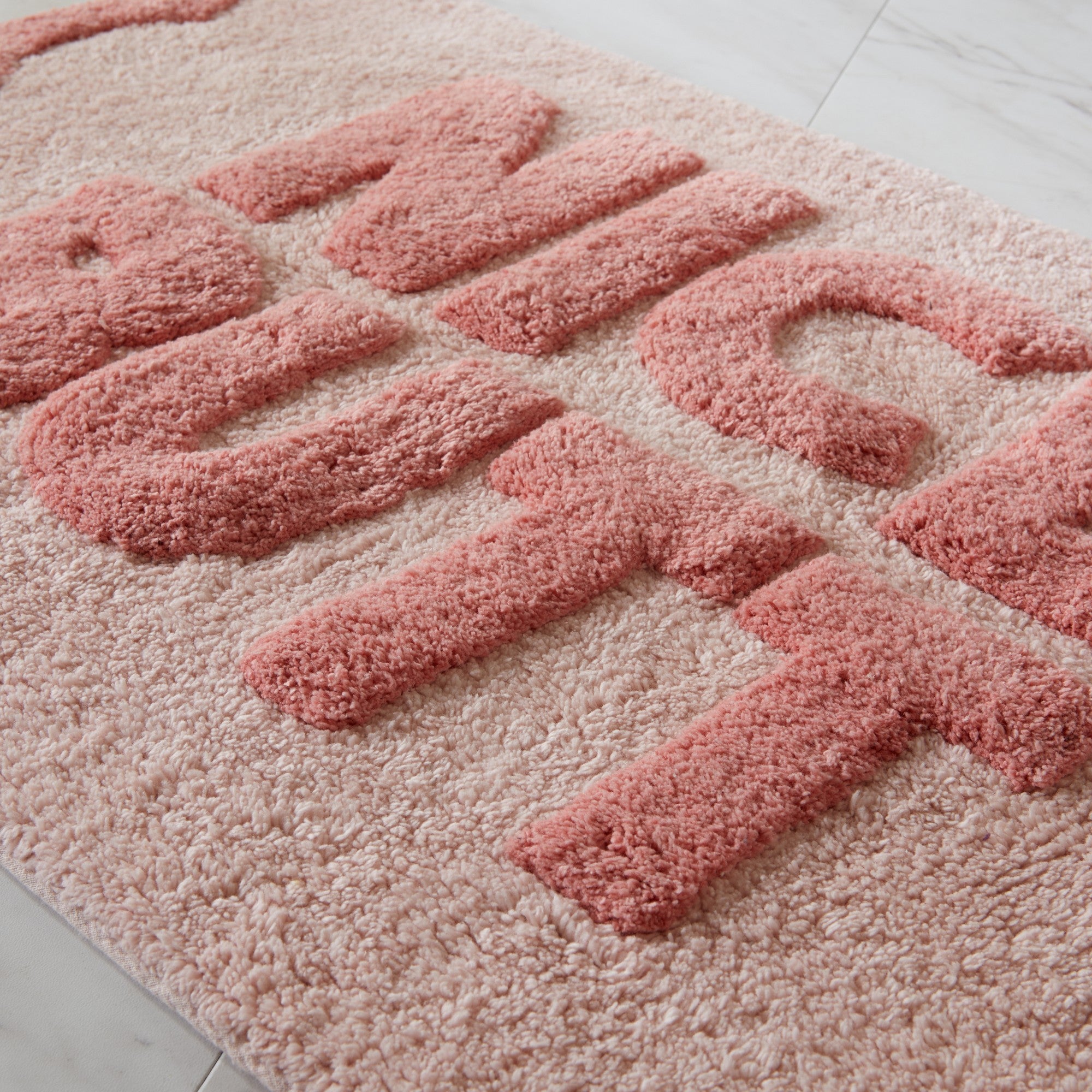 Pink doormat with 'NICE BUTT' text on a light gray floor.