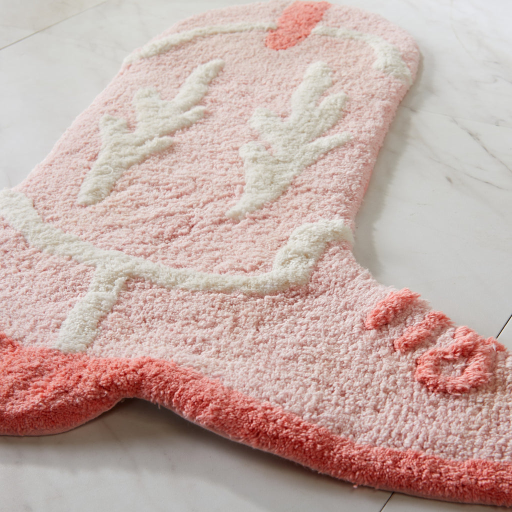 Pink bath mat with white floral design on a light gray floor