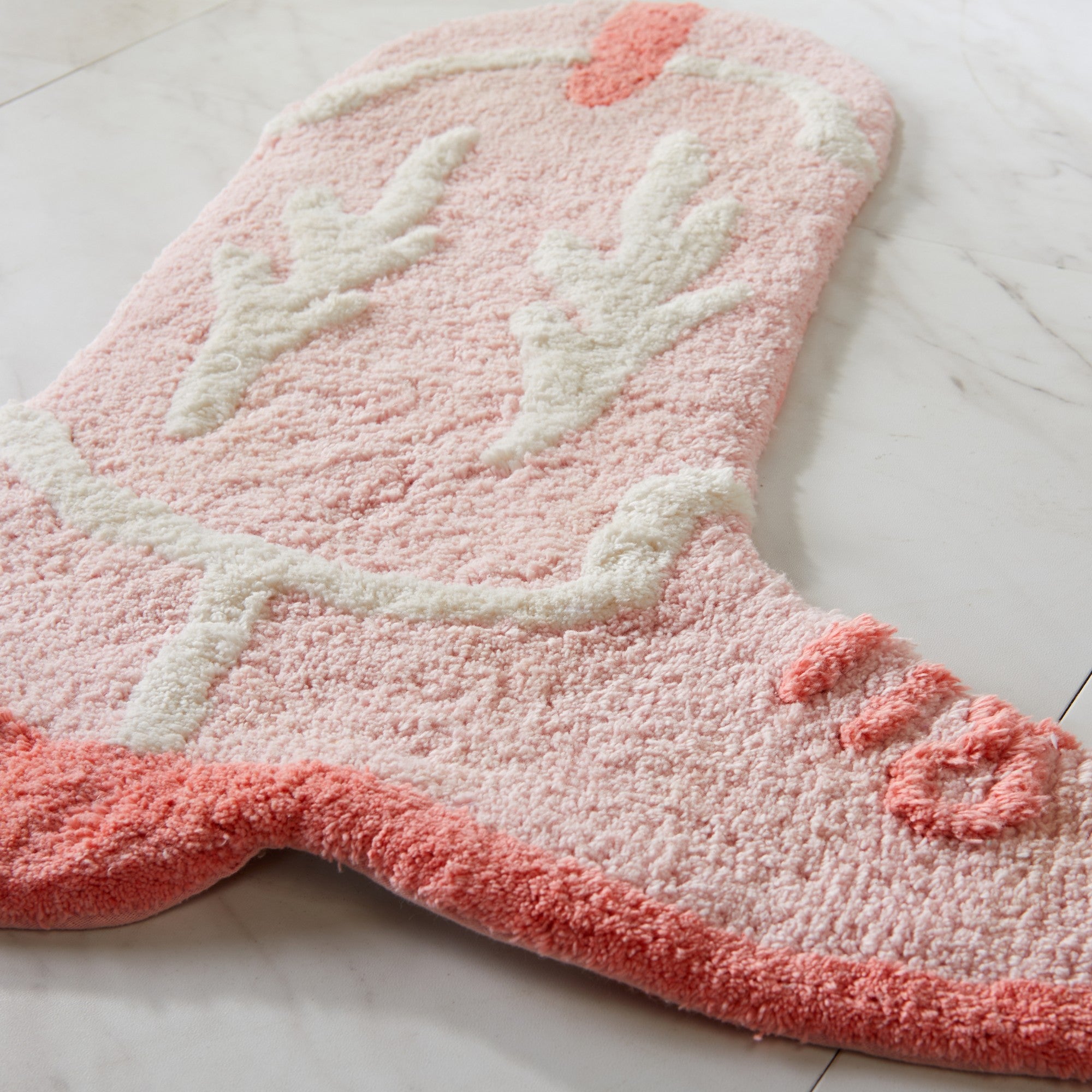 Pink bath mat with white floral design on a light gray floor