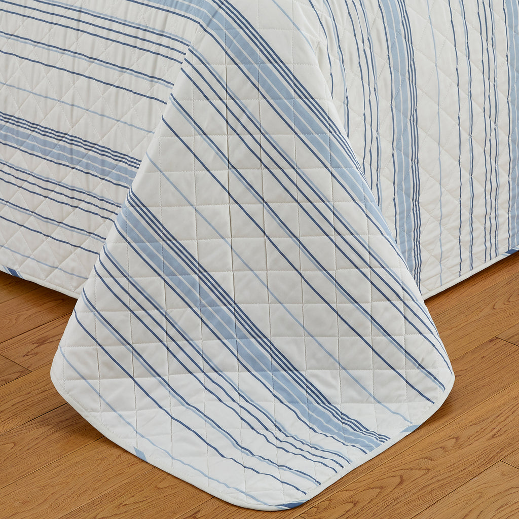 Sofia Collection striped quilt set featuring classic blue and white stripes with a reversible design, shown on beds and in close-up detail views. Soft, lightweight bedding with coordinating shams, styled in a bright and casual bedroom setting.