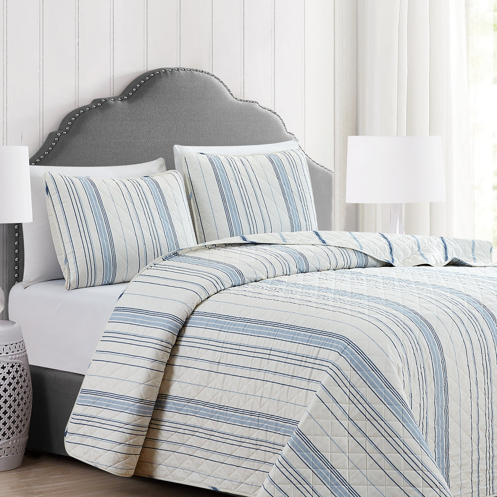 Sofia Collection striped quilt set featuring classic blue and white stripes with a reversible design, shown on beds and in close-up detail views. Soft, lightweight bedding with coordinating shams, styled in a bright and casual bedroom setting.