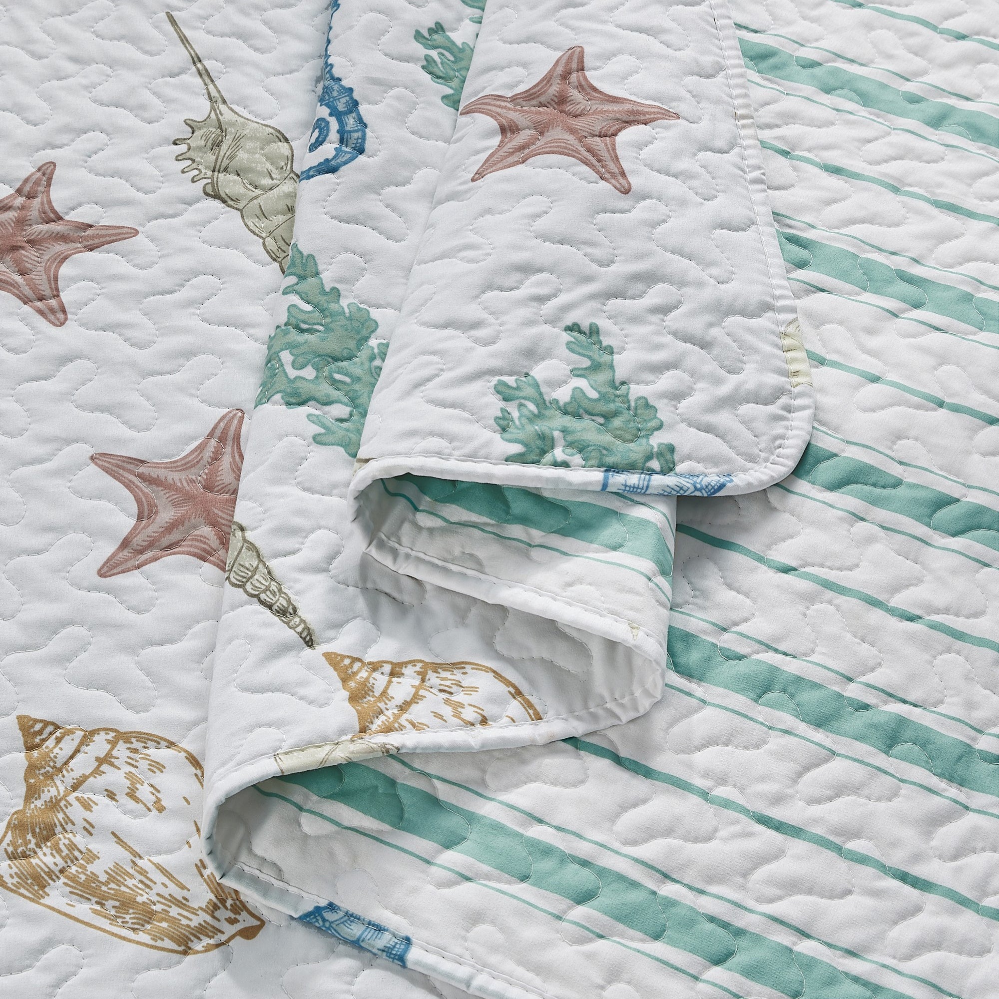 Coastal Collection Reversible Quilt Set by Market & Place featuring soft microfiber construction and coastal-inspired prints, including seashells, starfish, seahorses, coral, and ocean motifs. Coordinating shams and detailed fabric close-ups are shown in a bright bedroom setting, highlighting the reversible design and all-season comfort.