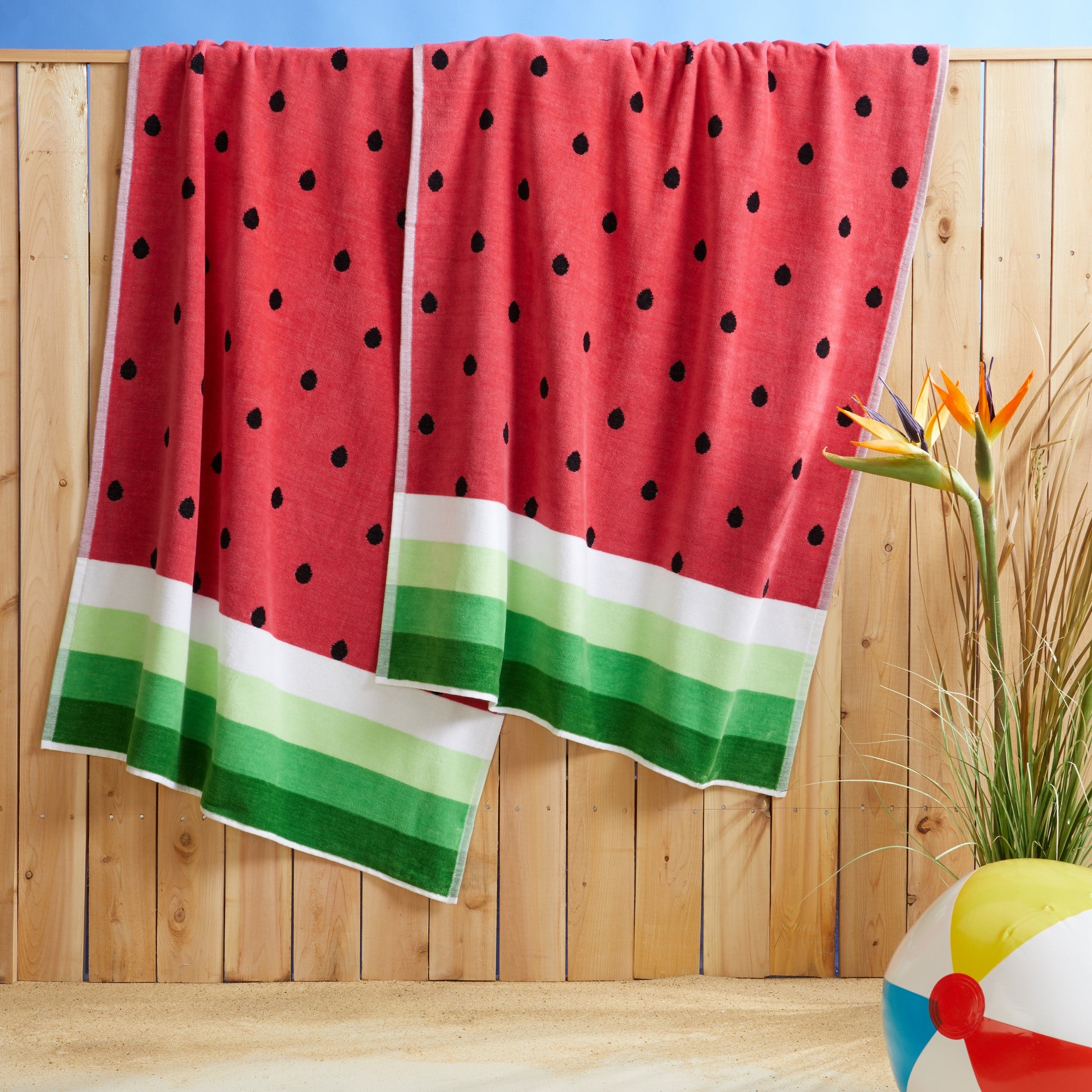 100% cotton velour beach towel featuring a colorful jacquard design, displayed on a wooden deck. Soft, absorbent, and durable, perfect for beach days, poolside lounging, and summer travel.