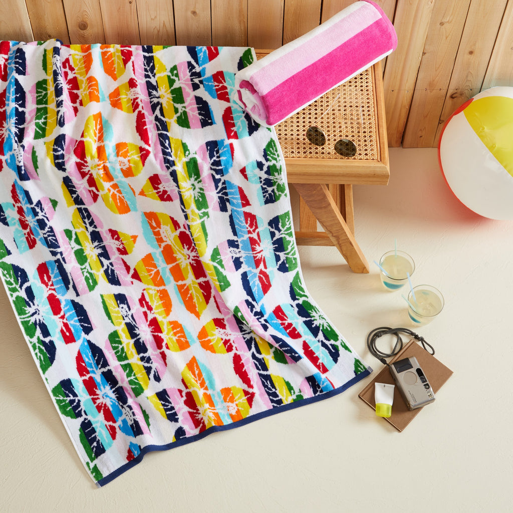 100% cotton velour beach towel featuring a colorful jacquard design, displayed on a wooden deck. Soft, absorbent, and durable, perfect for beach days, poolside lounging, and summer travel.