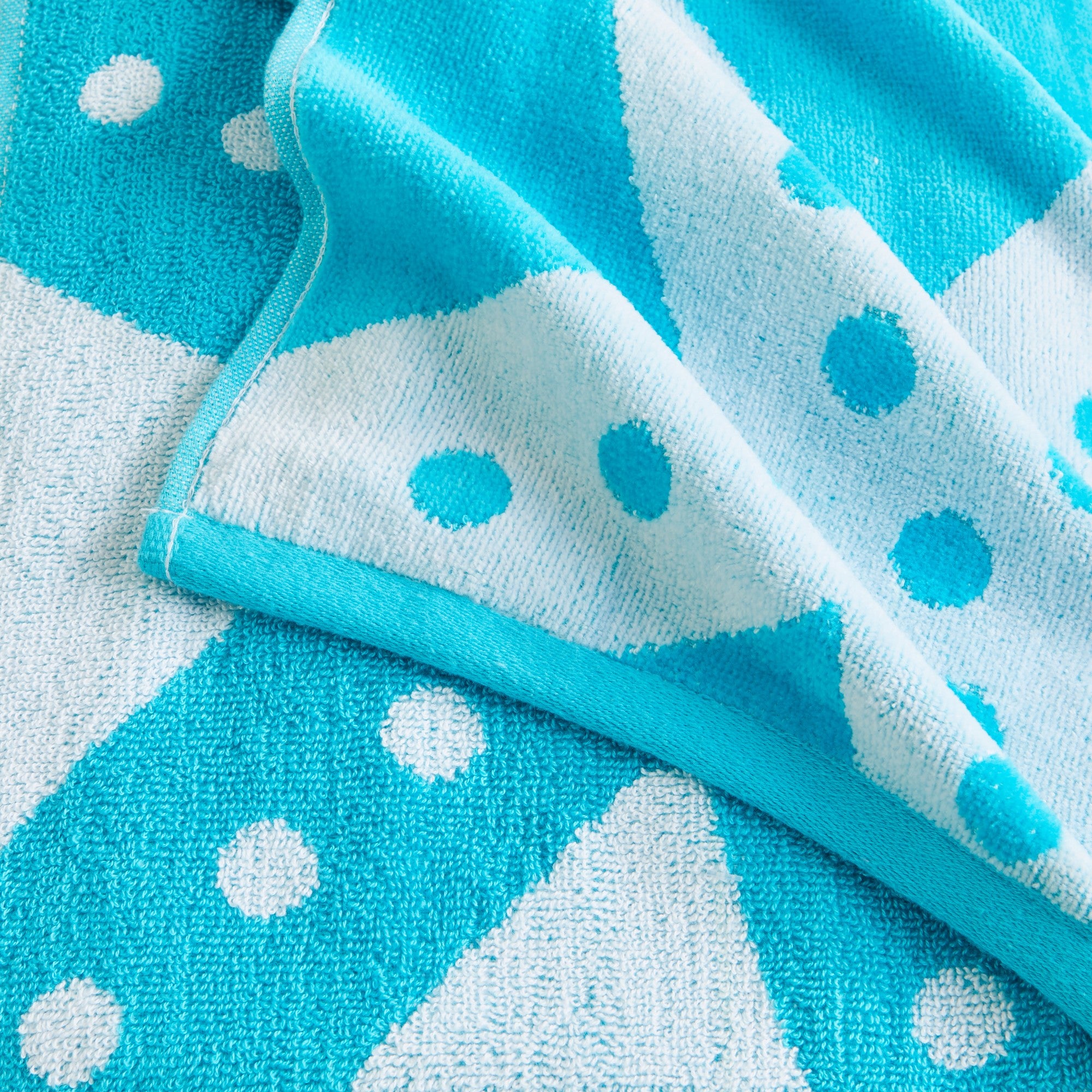 100% cotton velour beach towel featuring a colorful jacquard design, displayed on a wooden deck. Soft, absorbent, and durable, perfect for beach days, poolside lounging, and summer travel.