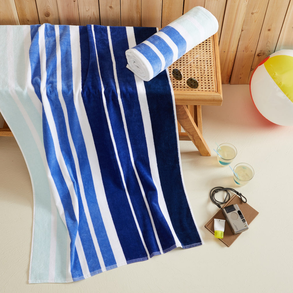 100% cotton velour beach towel featuring a colorful jacquard design, displayed on a wooden deck. Soft, absorbent, and durable, perfect for beach days, poolside lounging, and summer travel.