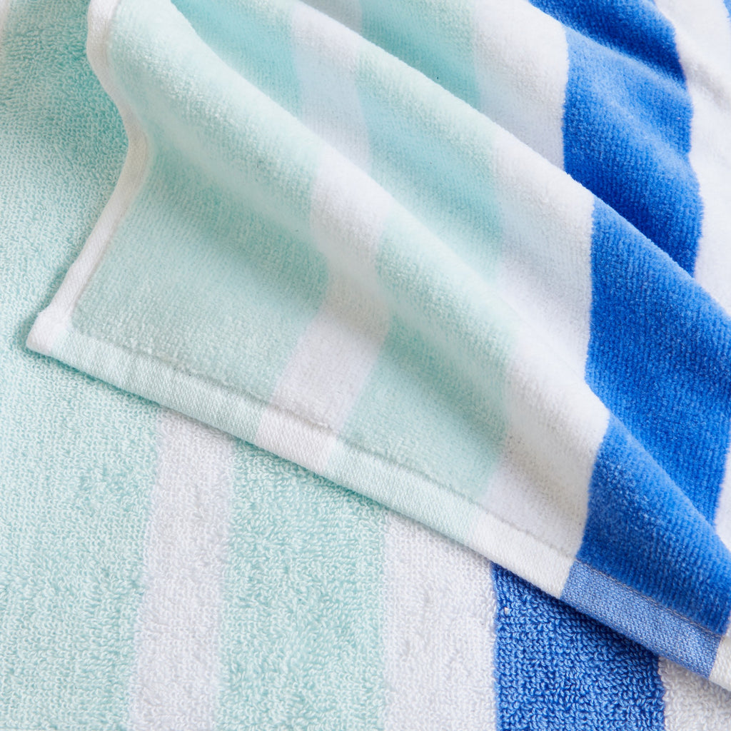 100% cotton velour beach towel featuring a colorful jacquard design, displayed on a wooden deck. Soft, absorbent, and durable, perfect for beach days, poolside lounging, and summer travel.