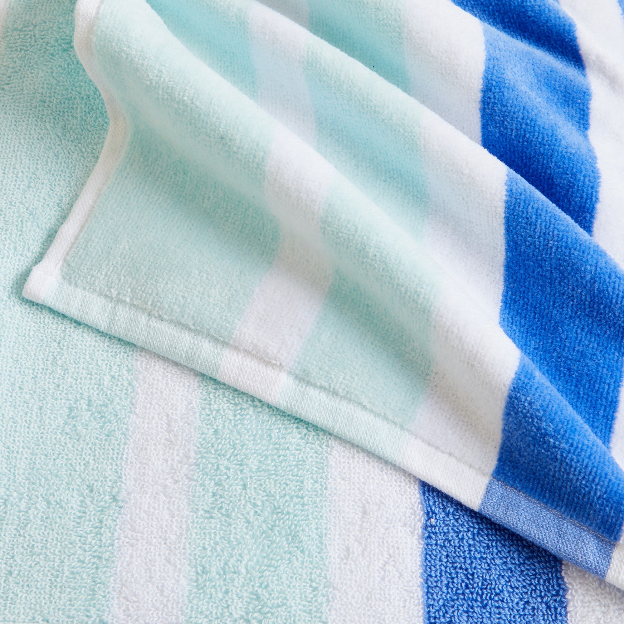 100% cotton velour beach towel featuring a colorful jacquard design, displayed on a wooden deck. Soft, absorbent, and durable, perfect for beach days, poolside lounging, and summer travel.